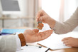 © New Africa - Real estate agent giving key with trinket to client in office, closeup