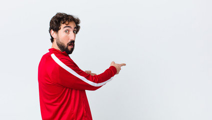 Poster - young bearded man back view feeling shocked and surprised, pointing to copy space on the side with amazed, open-mouthed look against copy space wall