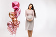 © SDammer - A young beautiful pregnant girl is posing and having fun on a white background with a large bunch of shiny balloons. Valentine's day, bachelorette party, March 8, baby shower.
