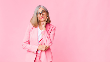 middle age cool woman smiling happily and daydreaming or doubting, looking to the side against flat wall