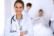 © rogerphoto - Female doctor smiling on the background with patient in the bed and two doctors