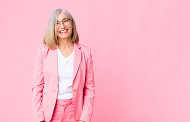 Wall Mural - middle age cool woman with a big, friendly, carefree smile, looking positive, relaxed and happy, chilling against flat wall