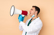 © luismolinero - Young dentist man holding tools isolated on beige background shouting through a megaphone