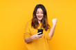 © luismolinero - Young caucasian woman isolated on yellow background with phone in victory position