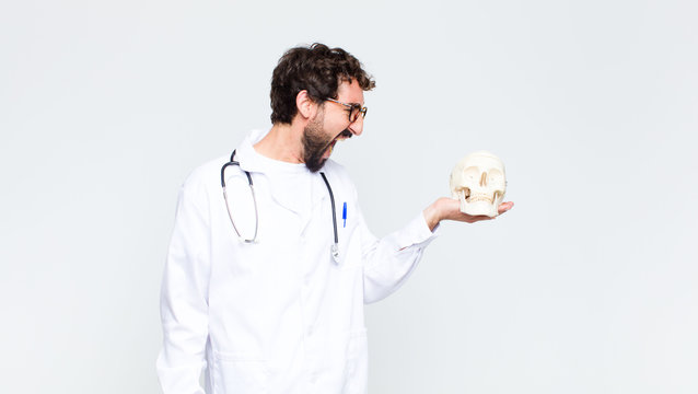 young crazy bearded doctor man holding a human skull