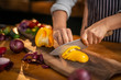 © TheSupporter - Female chef is slicing a delicious, fresh yellow pepper on wooden board in a restaurant or kitchen.