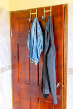 Half Worn Clothes Hanging On Stainless Steel/ Chrome Metal Over The Door Hooks On Inside Of Bathroom/ Bedroom/ Room Door. Female Child/ Adult Lady's/ Woman's Hoodie Sweater And Jeans Shorts Clothing.