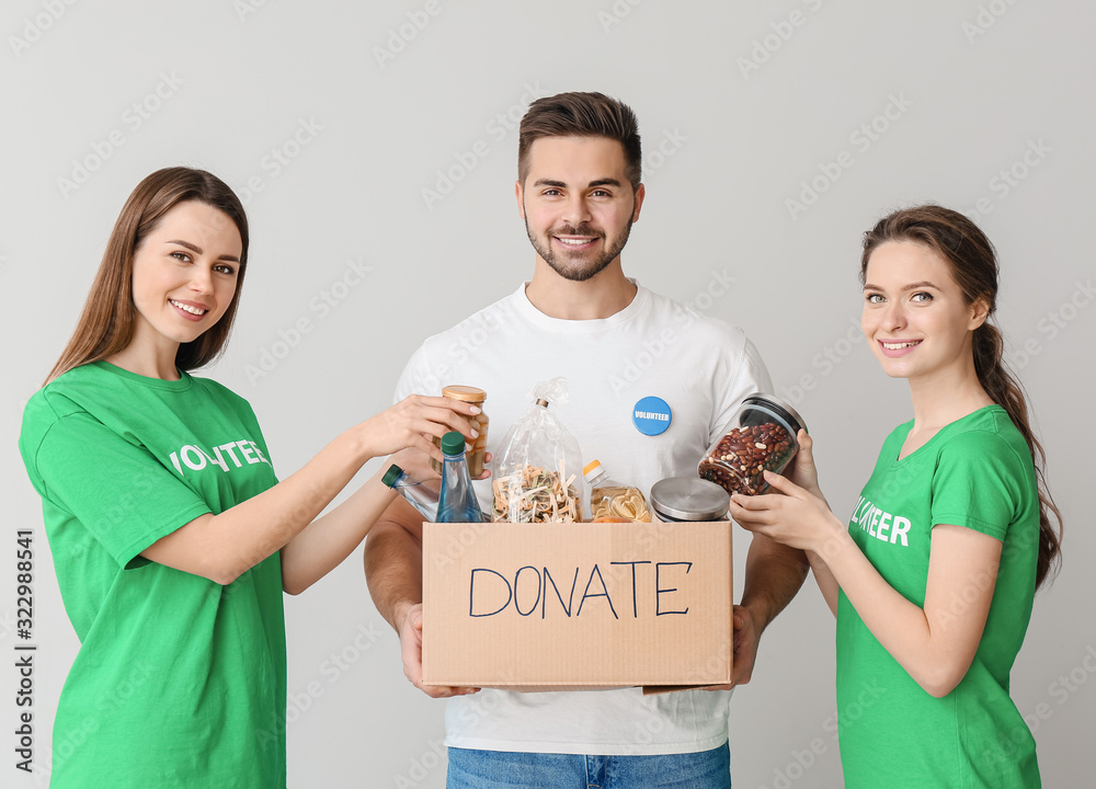 Volunteers with donations for poor people on light background