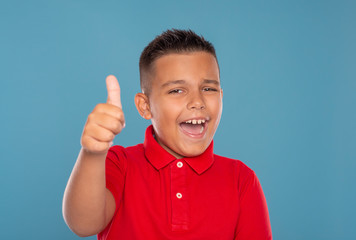 A young laughing boy   givs you an approving gesture against blue background with copy space