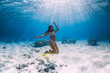 © artifirsov - Woman glides underwater with yellow fins over sandy sea and coral.