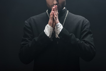 Wall Mural - cropped view of young catholic priest praying isolated on black