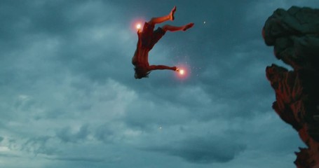 extreme sports stunt man backflipping off of a sea cliff into the ocean with burning hot red flares,
