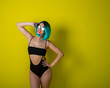 © Михаил Решетников - Beautiful woman in a black bikini in a colored wig and sunglasses on a yellow background. Girl posing in the studio.