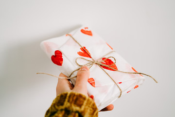 Wall Mural - a gift in a woman's hand wrapped in homemade wrapping paper with red hearts tied with jute thread for Valentine's day