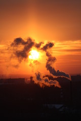 Wall Mural - red sun at sunset or dawn at dusk low above the horizon shrouded in smoke from the chimneys of the p