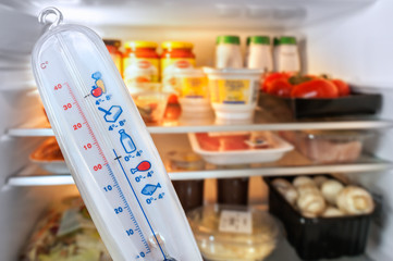 Thermometer in front of open fridge / refrigerator filled with food in kitchen