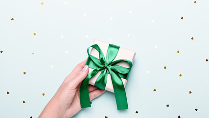 woman holding gift box in green color on pastel blue background with heart shape confetti, copyspace