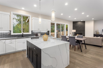 Kitchen and living room interior in new luxury home with open concept floor plan. Features island, hardwood floors, fireplace, dining area, and light filled spaces.