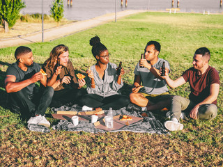 Relaxed young people cheering with beer bottles. Happy friends resting in summer park. Concept of celebration