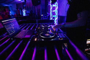 Wall Mural - DJ plays live set and mixing music on turntable console at stage in the night club. Disc Jokey Hands on a sound mixer station at club party. DJ mixer controller panel for playing music and partying.