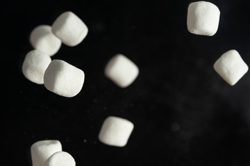 Falling marshmallows on a black background. Background of sweets for design, freezing in motion.