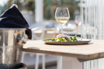 Dish of fish with vegetables served in a wood table with wine glasses and a bottle of wine in a terrace