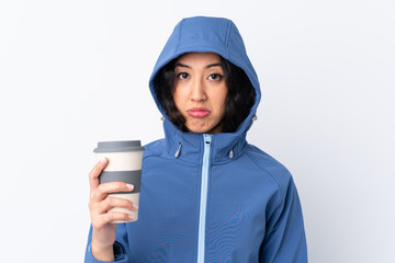 Wall Mural - Mixed race woman wearing winter clothes with the hood on and holding a hot takeaway coffee over isolated white background with sad expression