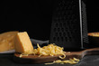 Delicious grated cheese on wooden board against black background
