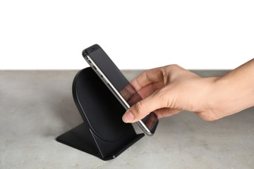 Woman putting mobile phone onto wireless charger at  grey table, closeup