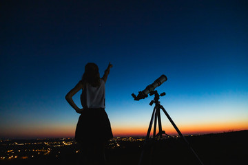 Wall Mural - astronomer with a telescope watching at the stars and moon with blurred city lights in the backgroun