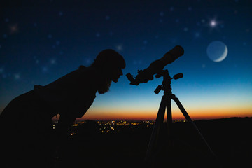 Wall Mural - astronomer with a telescope watching at the stars and moon with blurred city lights in the backgroun