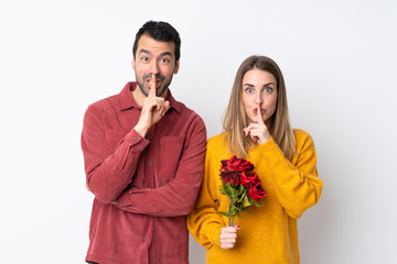 Couple in Valentine Day holding flowers over isolated background showing a sign of silence gesture putting finger in mouth