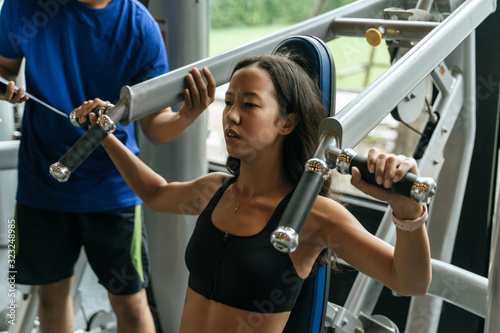 asian young sporty woman exercising chest press machine with personal trainer for perfect body in fitness gym, bodybuilder, healthy lifestyle, exercise fitness, workout and sport training concept