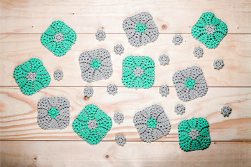 Lot of knitted gray-green, square napkins on the background of light wooden table. Crochet. Elements of needlework