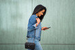 © mimagephotos - Side of smiling young latin woman walking with mobile phone and purse