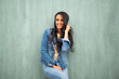 © mimagephotos - attractive young latin woman smiling by green wall with hand in hair
