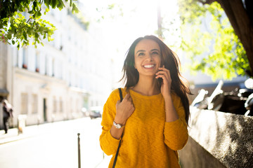 Wall Mural - Close up smiling young hispanic woman walking and talking with cellphone in city