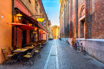 Fototapete - Cozy street with old houses and tables of restaurant in Ferrara, Emilia-Romagna, Italy. Ferrara is capital of the Province of Ferrara.