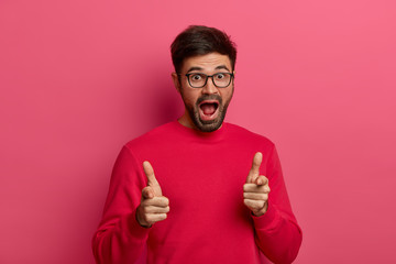 Wall Mural - Hey, you. Charismatic excited unshaven man points directly at you, keeps mouth opened, expresses choice, satisfied what he sees, dressed in casual wear, appealing to potential client, isolated on pink