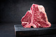 Raw dry aged wagyu porterhouse beef steak with large fillet piece as closeup on a black burnt wooden board with copy space left