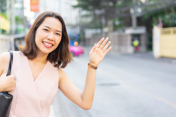 close up young employee woman raising hand to call on taxi car to get on for go to work in the rush time , city life concept