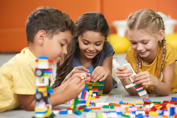 Happy kids playing with constructor at kindergarten. Children playing with colorful plastic bricks on the floor. Preschool kids having fun.