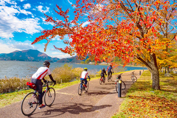 Wall Mural - Kawaguchiko. Japan. Bike riders ride along the promenade. Yagizaki Park. Men on the background of Lake Kawaguchiko. Japan tour. Group of Tourists in Fujikawaguchiko. Japan on an Autumn Day.