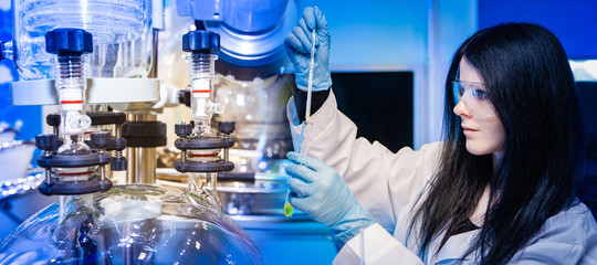 Poster - a girl in safety glasses and rubber gloves on the background of a bioreactor. the microbiologist exa