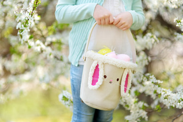 Close-up of little girls hands holding cute Easter basket in blooming cherry garden on beautiful spring day. Kid hunting for Easter eggs on Easter day.