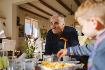 Portrait of old senior man pensioner grandfather sitting at the restaurant looking to his caucasian grandson son boy child taking food family nursery