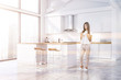 © ImageFlow - Woman with phone in white kitchen with bar