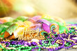 canvas print picture - Happy Mardi Gras text in gold glitter and a king cake with yellow, green, and purple sprinkles surrounded by Mardi Gras beads and a glittering fleur de lis.