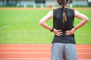 Back view of young runner woman suffering from Backache or Sore waist after running in the running track in stadium. Conceptual of woman suffering painful from sport workout.