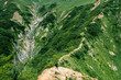 © ryo_k12 - Hiking trail along a steep green mountain ridge with small hikers